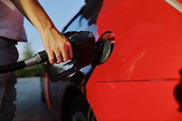 A woman's hand holds a petrol pump inserted into a red car.